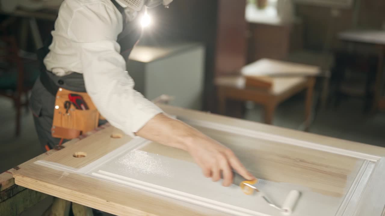 primer plano de manos masculinas con un rodillo pintando la puerta en blanco