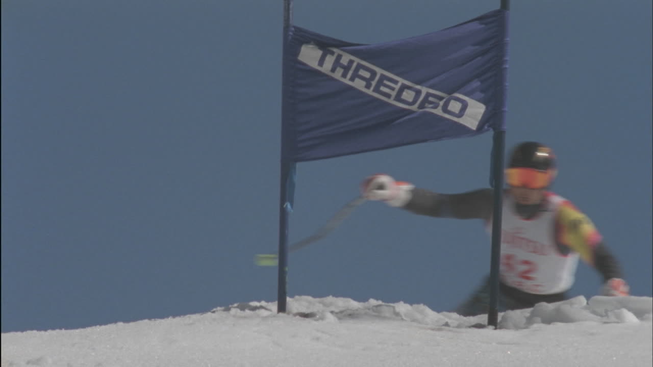 경쟁적인 스키 선수가 내리막 스키를 타면서 표지판을 통과합니다.