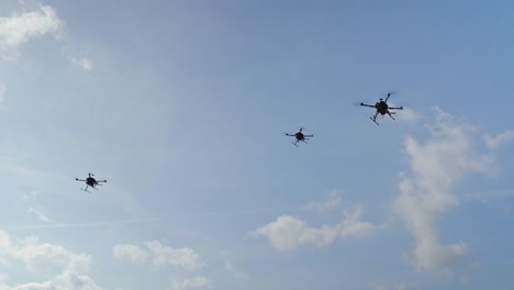 three military drones hovering in the air against blue sky and clouds