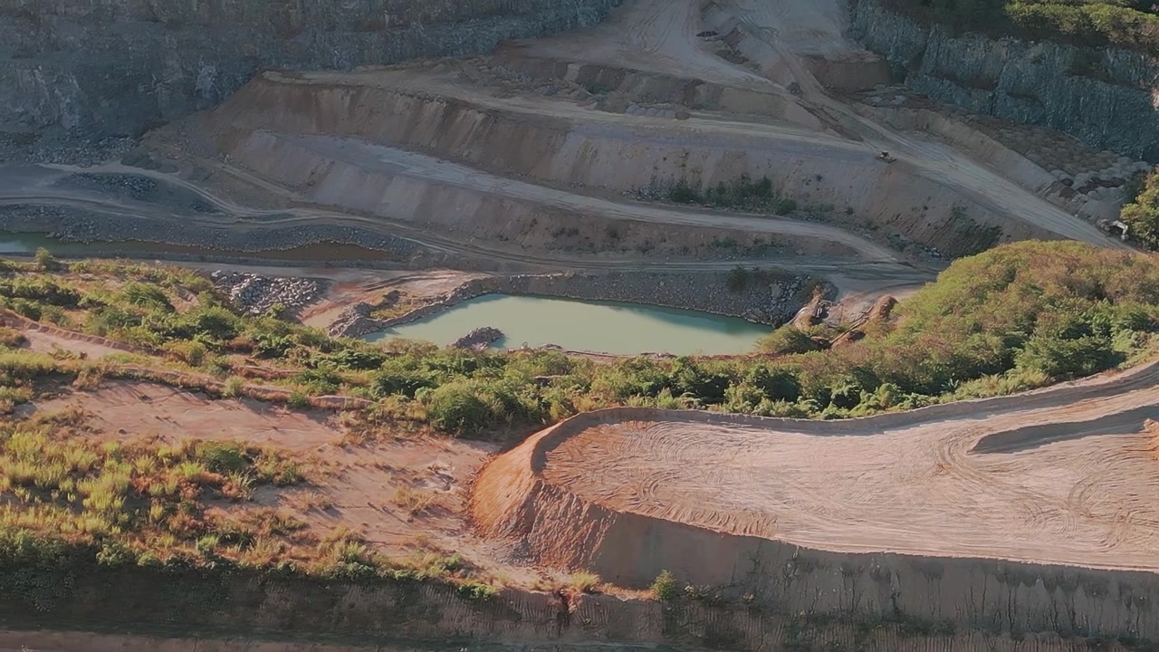 Terraced limestone quarry with haul roads, excavation benches and sediment pond in Fercal Brasília DF Brazil during drone lateral slide aerial shot