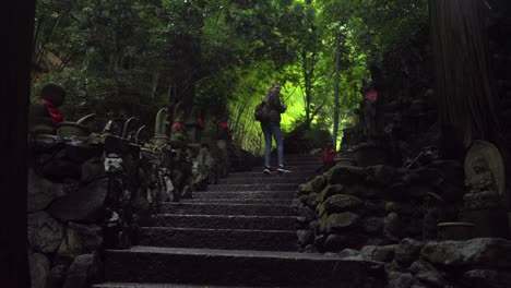 Beautiful-young-latin-woman-forest-path-way-to-Nanzoin-temple-at-Fukuoka-Japan-surrounded-of-Jizo-and-disciples-stone-statues-in-rainy-day