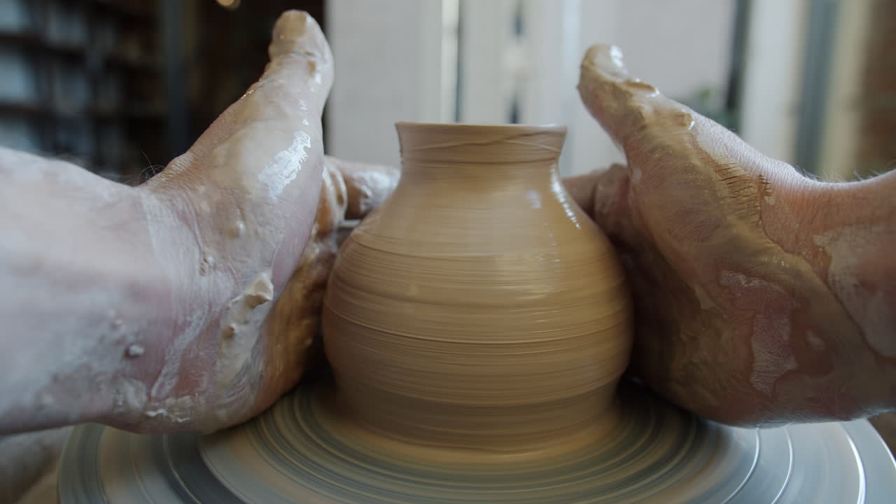 Hands shaping a clay pot on a pottery wheel
