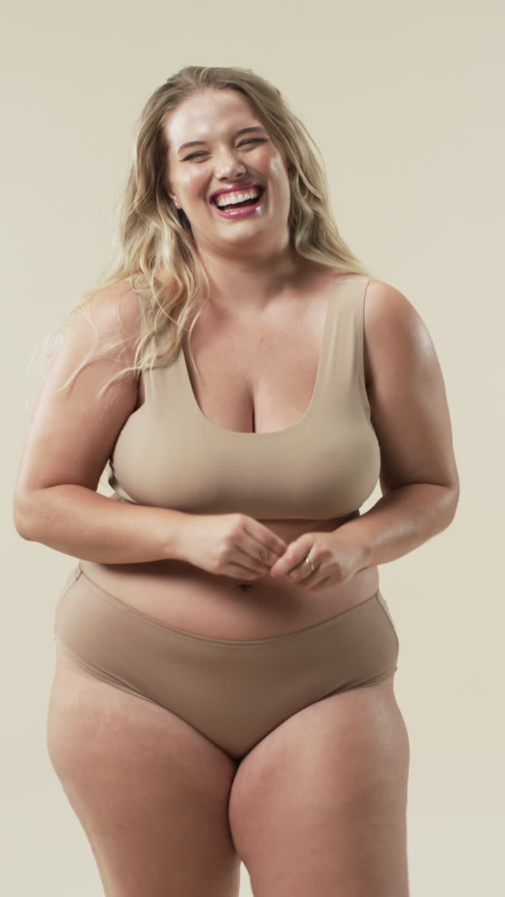 Video verticale: Donna curvy sorridente in intimo beige che promuove la body positivity.