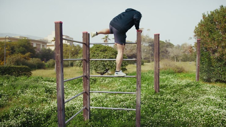 Man Trains on Iron Bars in the Park Surrounded by Nature