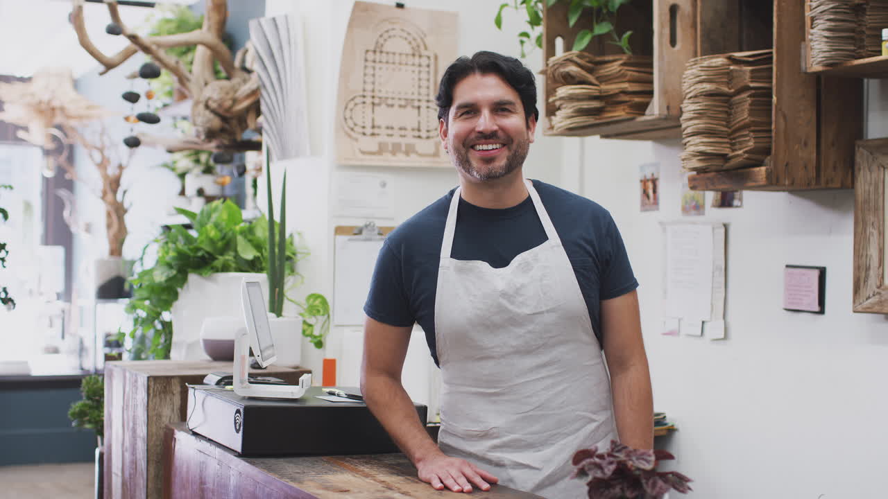 retrato de un asistente de ventas de sexo masculino sonriente de pie detrás del mostrador de ventas de la tienda de flores