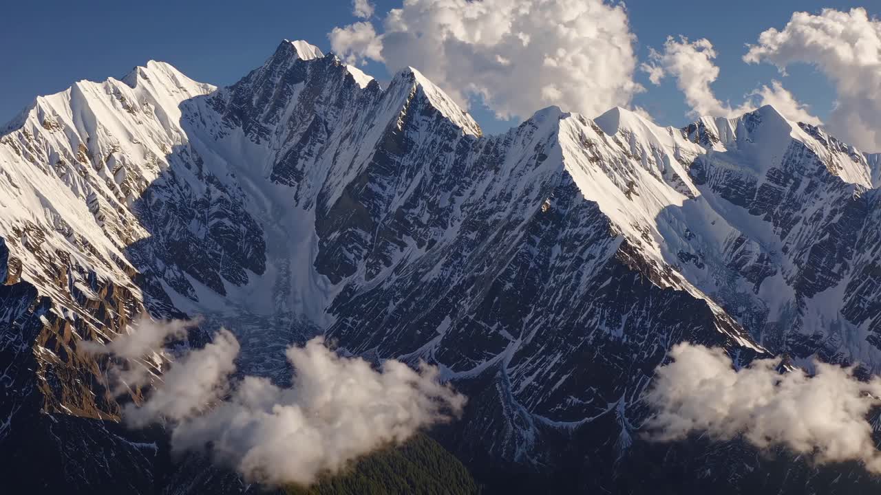 Aerial video captures majestic snow-capped mountains under a clear sky, with dramatic peaks