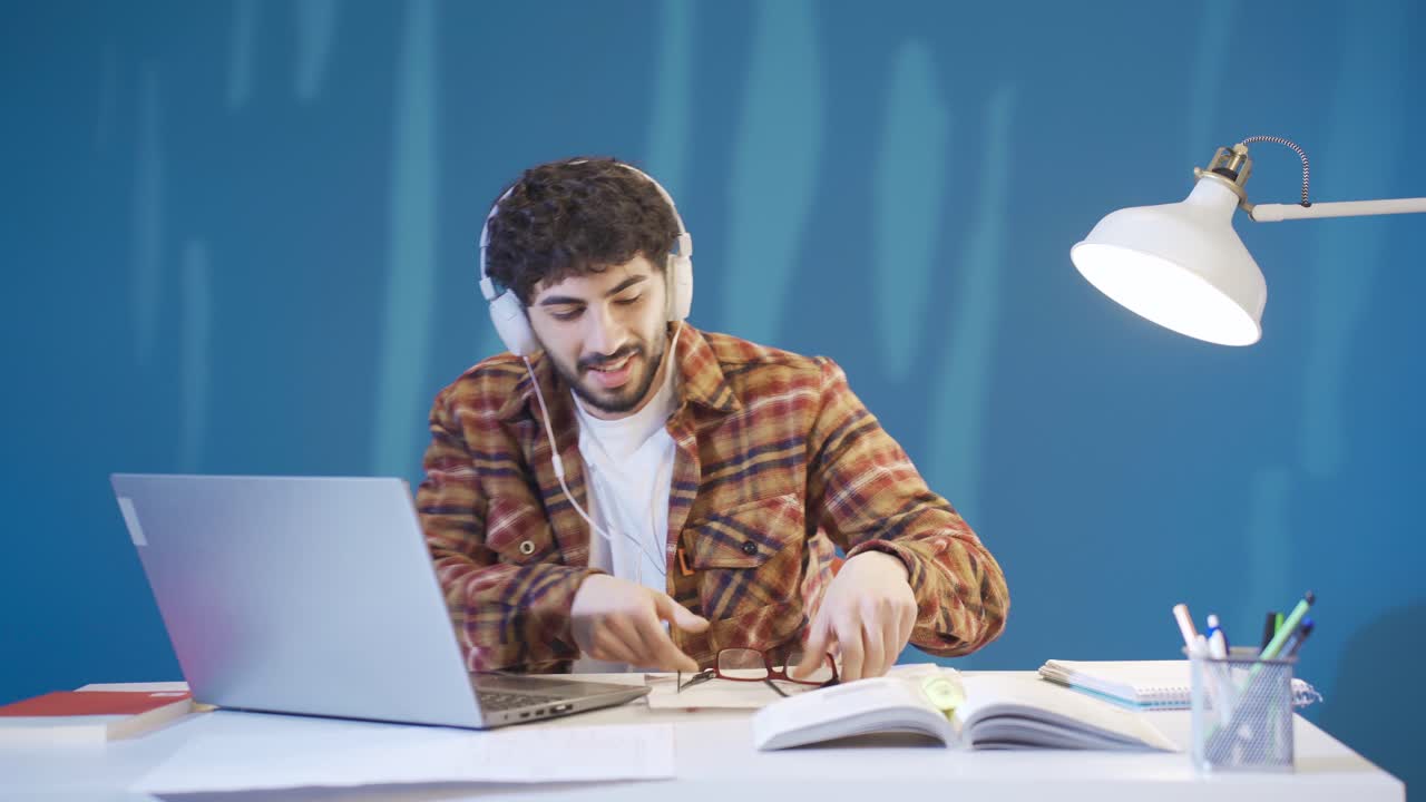 hombre joven guapo sentado en su escritorio, con auriculares, escuchando música y comenzando a estudiar.