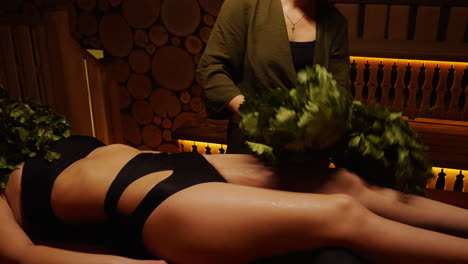 woman receiving a traditional sauna treatment with birch broom