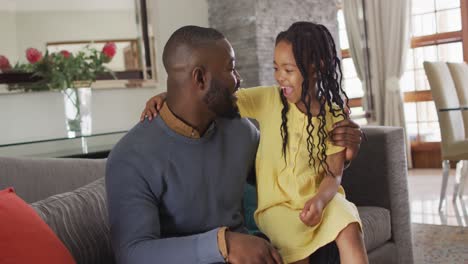 Happy-african-american-daughter-and-father-embracing-and-talking-on-sofa
