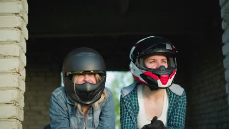 two women wearing helmets are leaning forward, the woman on the right seems to be looking at someone, while the other looks into the distance, both with intense expressions