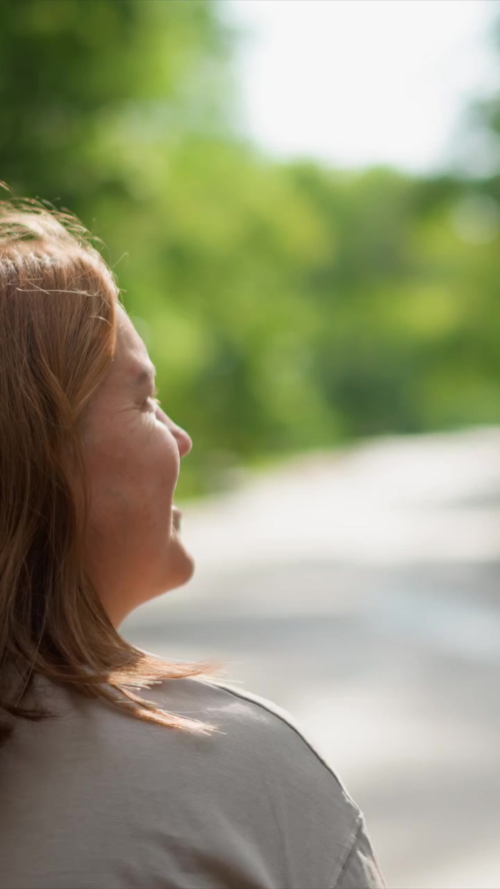 Il soggetto si muove in avanti tra uno sfondo naturale sfocato. I capelli si muovono leggermente mentre il soggetto rimane per lo più fermo. La luce naturale enfatizza i colori contro una pianta fuori fuoco.