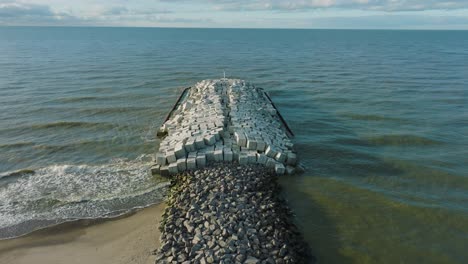 aerial establishing view of protective stone pier with concrete blocks and rocks at baltic sea coastline at liepaja, latvia, strengthening beach against coastal erosion, drone shot moving forward