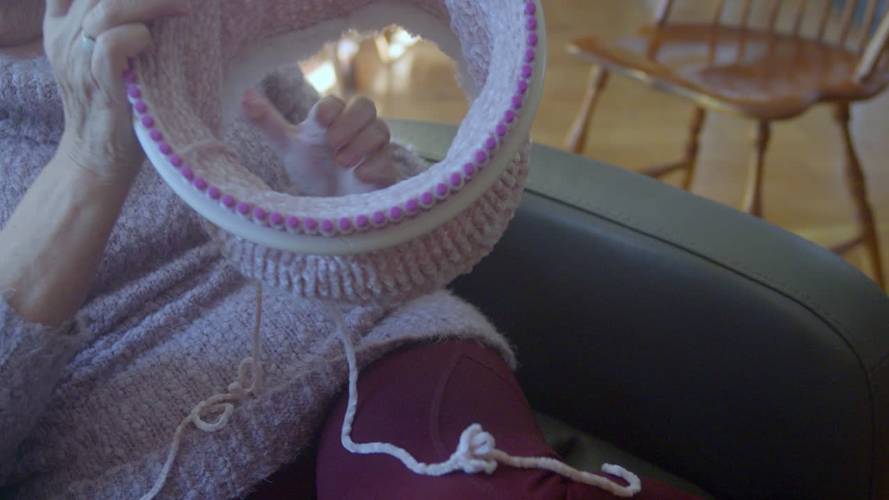 Circular knitting loom. Woman creates a knitted purple hat as she sits in a chair