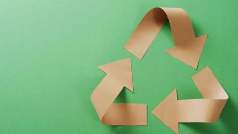 primer plano del símbolo de reciclaje de flechas de papel sobre fondo verde, con espacio para copiar