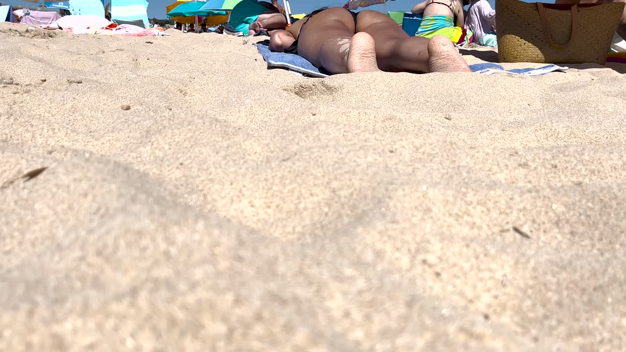 fit woman in a black bikini sunbathes amidst a crowd in Portugal, enjoying the sun