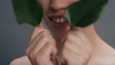 close up portrait beautiful mixed race woman smiling caressing face with leaf touching smooth healthy skin complexion enjoying natural skincare beauty on grey background