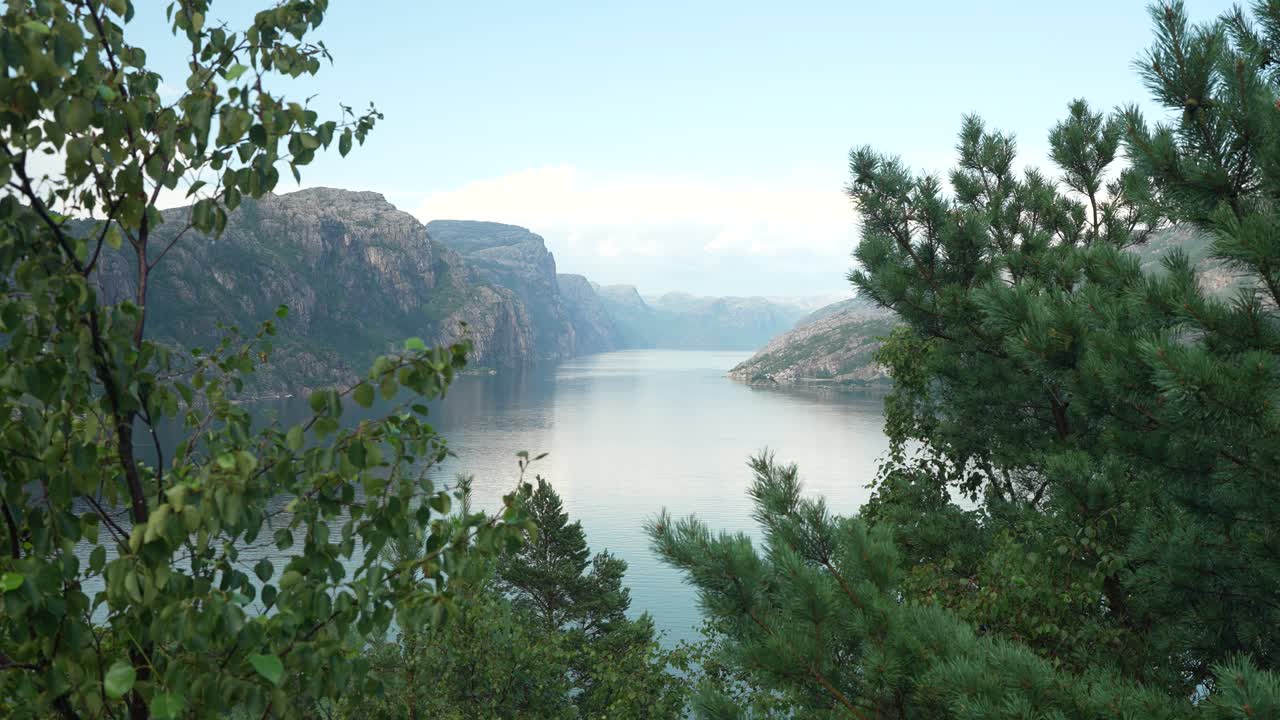 En lugn fjord speglar morgonhimlen med taggiga klippor som reser sig på båda sidor. Frodig grönska ramar in scenen och skapar en fridfull naturmiljö i Norges fantastiska landskap