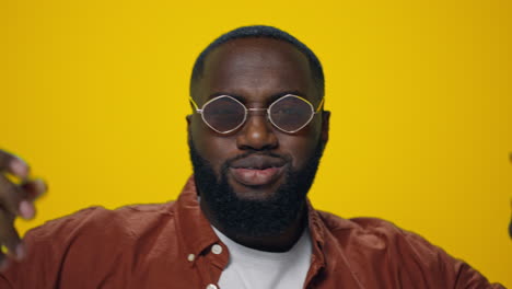 Cheerful-african-american-guy-in-sunglasses-dancing-in-yellow-background.