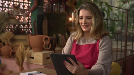 woman entrepreneur managing online orders of local flower shop. female store owner looking at tablet device writing order