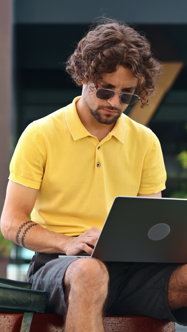 Man in yellow shirt talking standing on a bench and working on a laptop. Vertical
