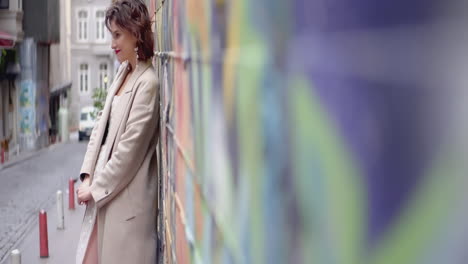 woman in beige coat leaning against a colorful wall