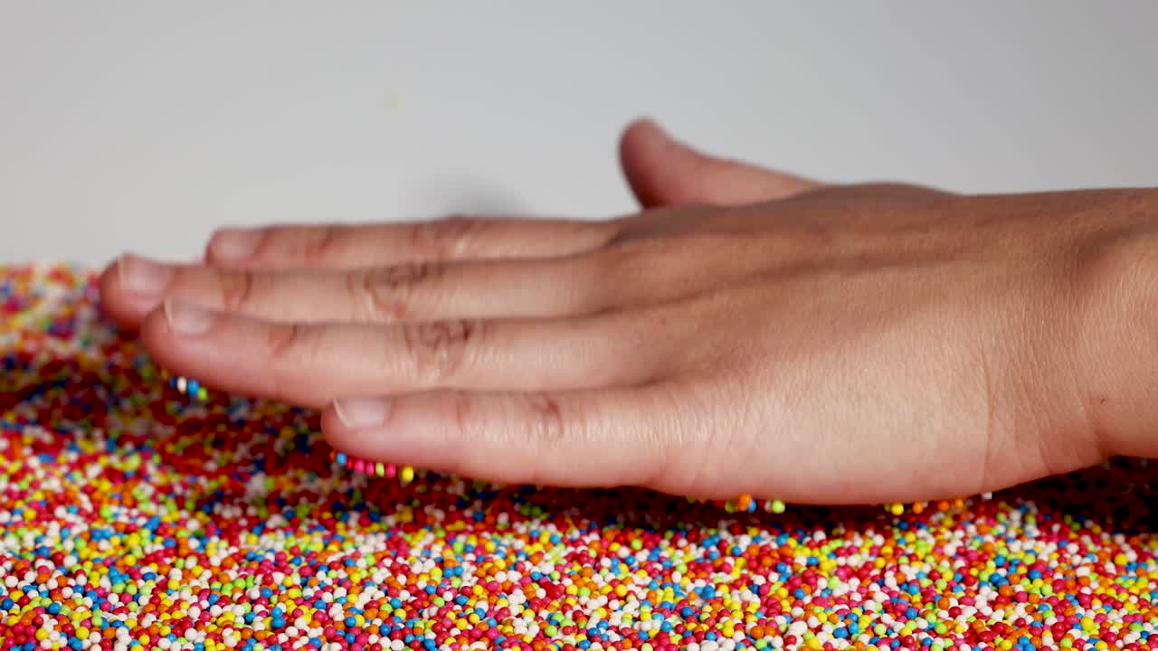 Hands gently press and release colorful sprinkles, creating a playful and tactile interaction in a well-lit environment