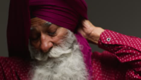 close up low key studio lighting shot of senior sikh man with beard tying fabric for turban against dark background 1