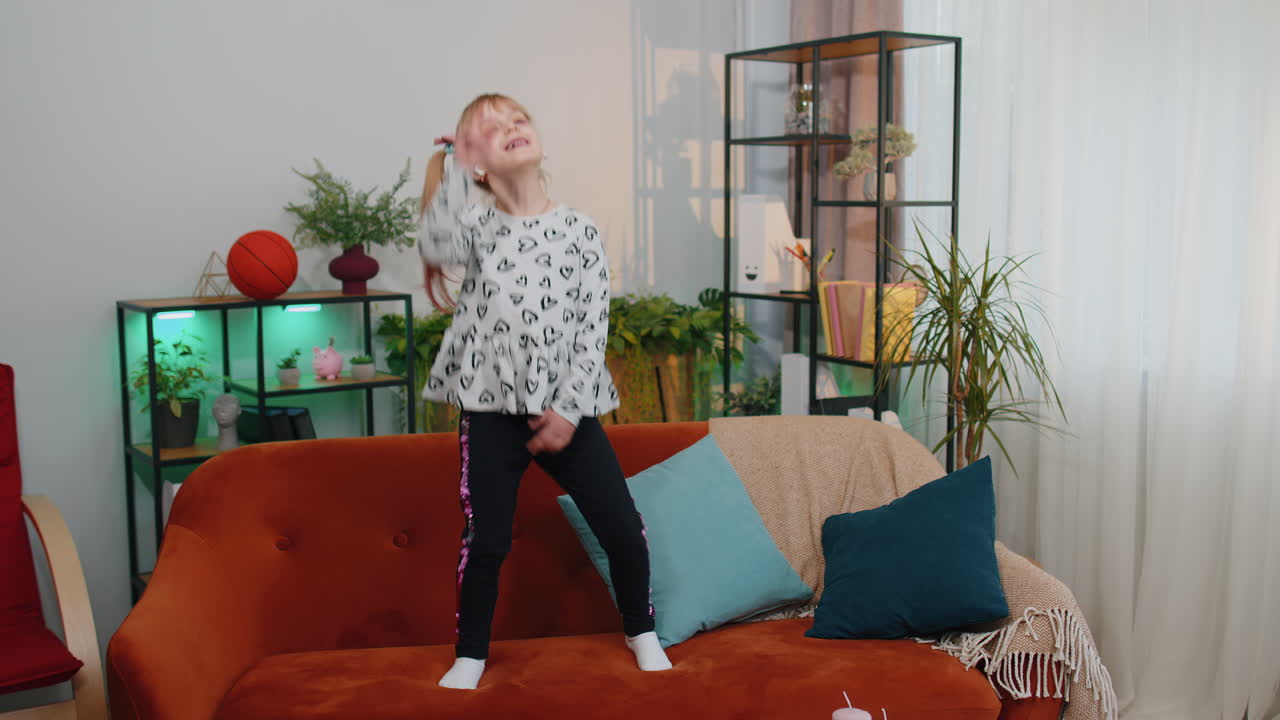 Happy child girl kid wears earphones dancing and jumping while listening to the music at home alone