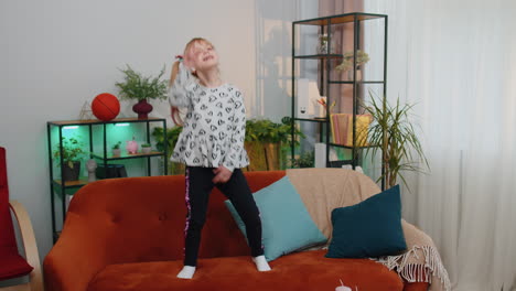 happy child girl kid wears earphones dancing and jumping while listening to the music at home alone