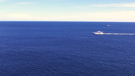 Drone-flying-towards-Speed-boat-sailing-across-vibrant-blue-sea-surface,-Pacific-Ocean