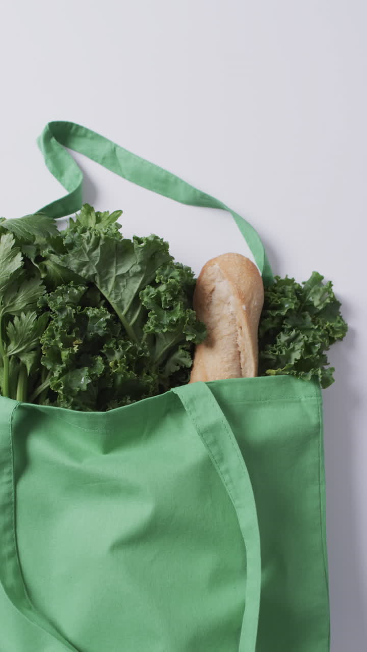 Vertical video of green canvas bag with parsley, kale and baguette, copy space on white background