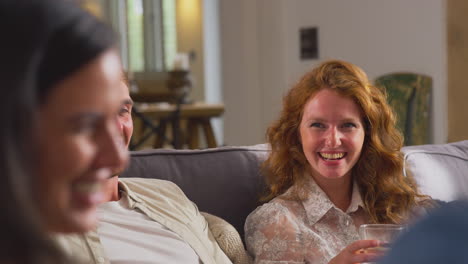 multi-cultural group of friends sitting on sofas at home together enjoying drinks and talking