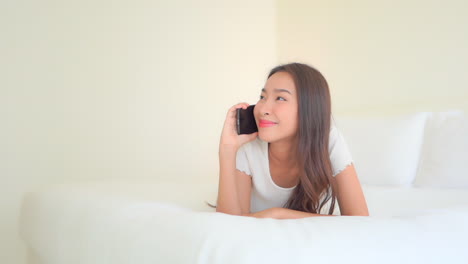 a pretty young woman lying on a comfortable hotel suite bed talking on her smartphone and reacting to what she hears