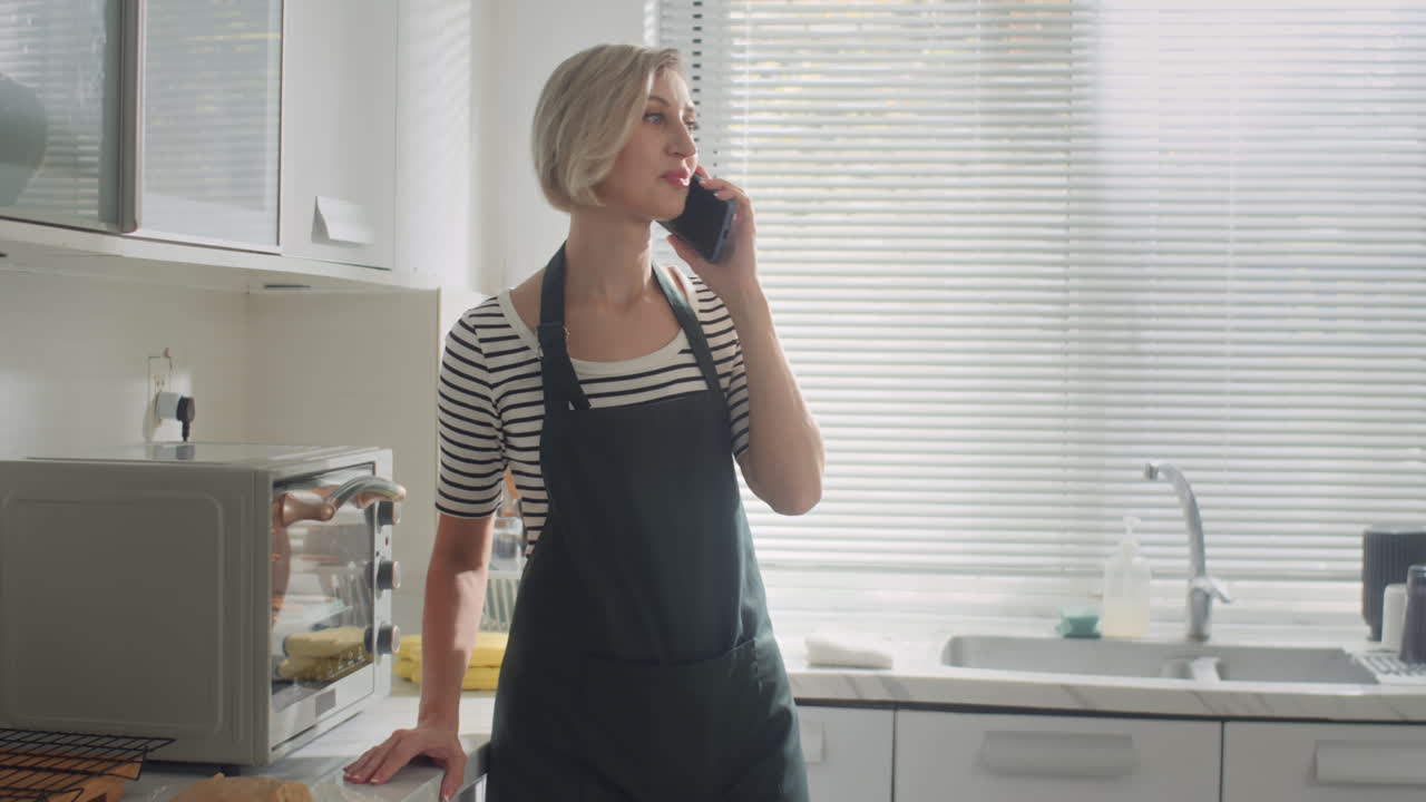 Housewife Talking on Smartphone when Cooking at Home Kitchen