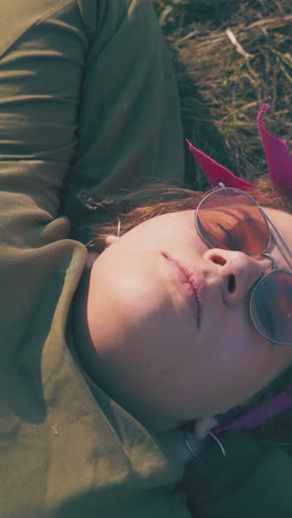 beautiful plump girl hiker with sunglasses lies on green grass at campsite in calm evening close view