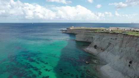 Malta's-Ras-il--Fenek-Limestone-Cliff-Side,-With-Tropical-Turquoise-Water,-Blue-Sky-And-Fluffy-White-Clouds