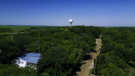 Un-Largo-Disparo-De-Drone-En-La-Cima-De-Un-árbol-Que-Se-Acerca-A-La-Histórica-Estructura-De-La-Torre-De-Agua-De-Trébol-De-Killarney,-Manitoba,-Junto-Al-Lago-Killarney-En-El-Oeste-De-Canadá.