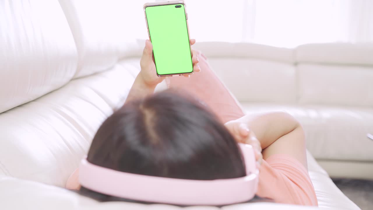 소파 에 휴대 전화 를 들고 음악 을 즐기는 여자