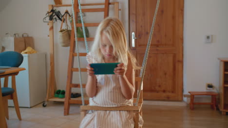 child swinging on indoor swing and using smartphone