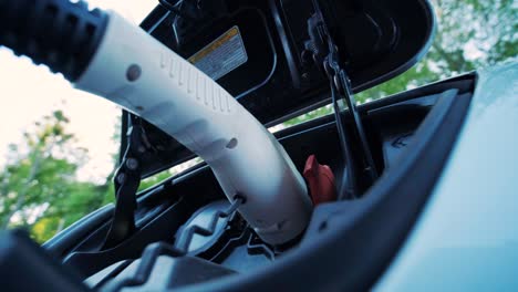 refueling process of an electric car. a shot under the hatch where the electric eco car charges. the electric car charging hatch opens automatically. a male hand inserts an erectile car