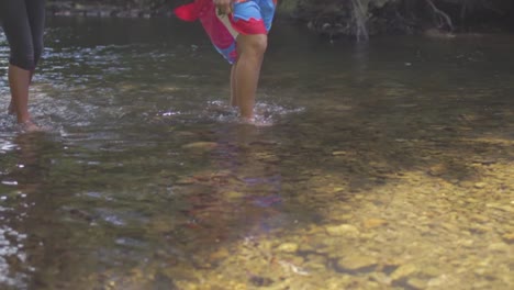 slow motion of two woman's feet walking in a shallow river in nature