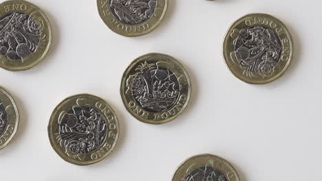 gold and silver british one pound coins laid flat on a white table - british money - overhead shot