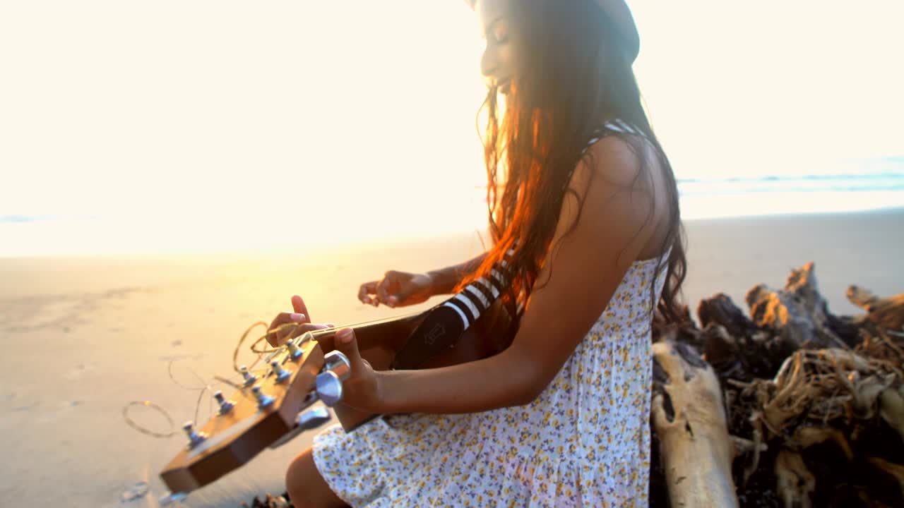 Donna indiano-americana che suona la chitarra su una spiaggia al tramonto