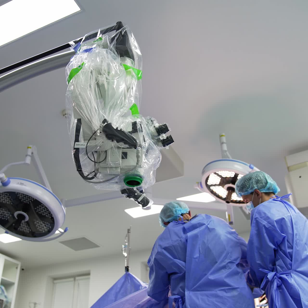 Stand with a big surgical microscope in operational room. Doctors conducting operation nearby. Low angle view
