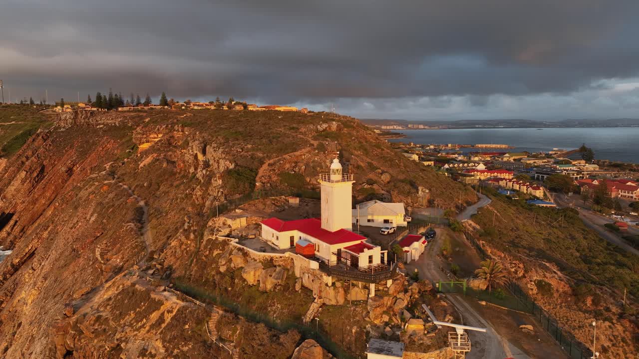 Ripresa aerea in allontanamento che svela il faro illuminato dall'ora d'oro a Mossel Bay, RSA