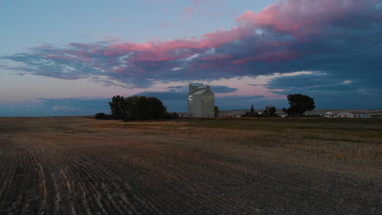 Ripresa aerea progressiva sopra un silos per cereali circondato su tutti i lati da campi agricoli al tramonto nel sud dell'Alberta, Canada.
