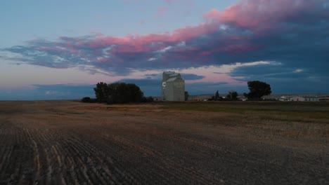 Disparo-De-Reenvío-Aéreo-Sobre-Un-Elevador-De-Granos-Rodeado-De-Campos-Agrícolas-Por-Todos-Lados-Al-Atardecer-En-El-Sur-De-Alberta,-Canadá