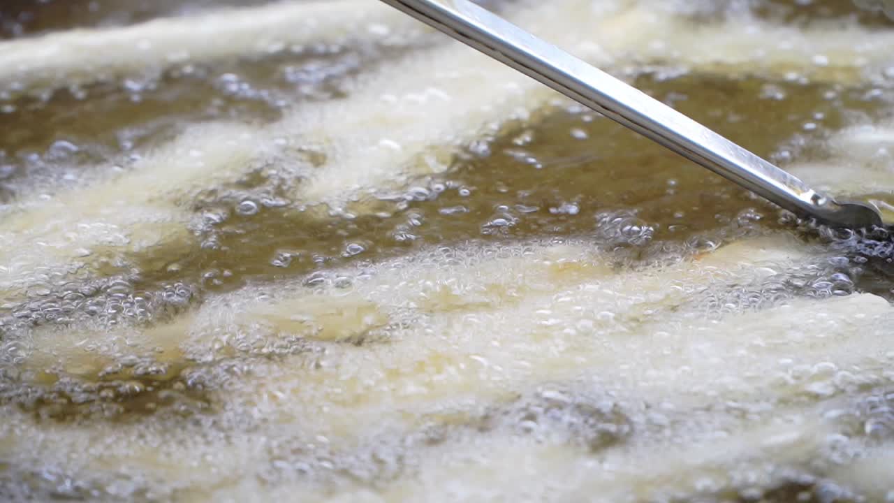 Using a kitchen clamp, churros in boiling oil are turned for even cooking.