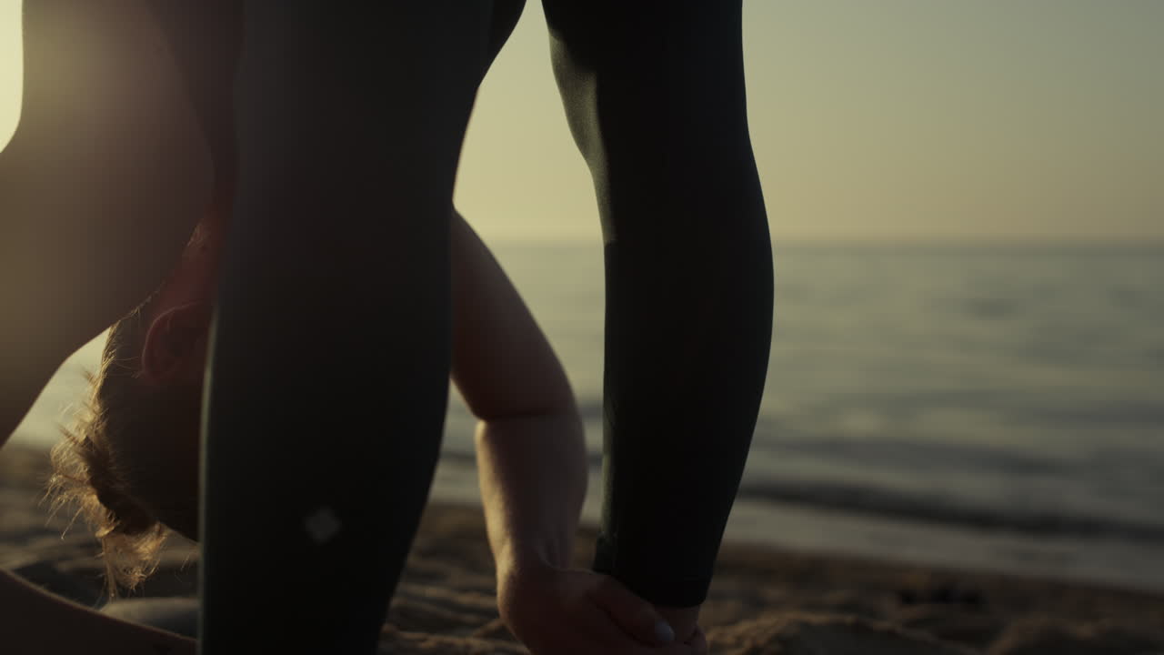 해변에서 스트레칭 운동을 하는 운동선수 소녀가 머리를 발로 기울이고 있습니다.