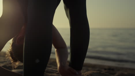 Athlete-girl-tilting-head-to-feet-making-stretching-exercises-on-beach-close-up.